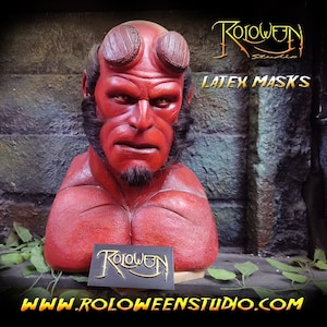 May include: Red latex mask of a character with horns, a beard, and a red and black painted chest. The mask is on a wooden base and the text "Roloween Studio Latex Masks" is visible in the background. The text "www.roloweenstudio.com" is visible in the foreground.