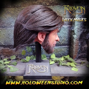 May include: A realistic latex mask of a man with long brown hair and a beard. The mask is mounted on a black stand with the word "Roloween" written on it. The text "Latex Masks" is also visible in the image.