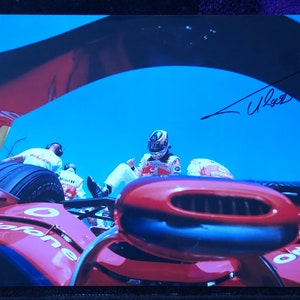 Può includere: Un'auto da corsa rossa con un pneumatico nero e un'aspirazione d'aria nera. L'auto è firmata da un pilota con il nome "Wurz".