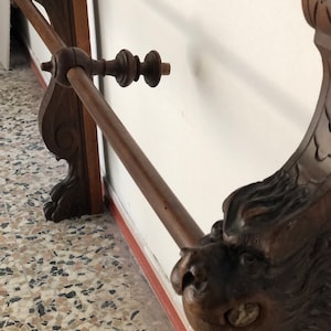 Puede incluir: Un perchero de madera con una cabeza de león tallada en un extremo y un remate decorativo en el otro. El perchero está montado en una pared y tiene un acabado marrón oscuro.