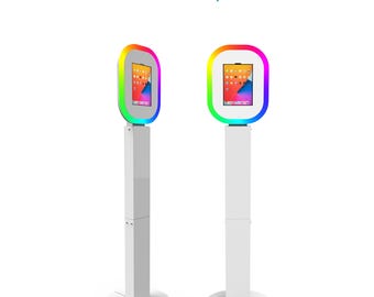 May include: Two white photo booth stands with a tablet mounted on each. The tablets have a rainbow colored ring light around them. The stands are adjustable in height and have a circular base.