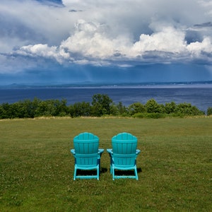 May include: Two turquoise blue Adirondack chairs facing a body of water with a cloudy sky in the background.