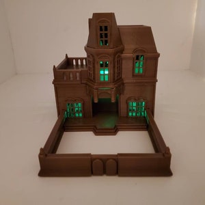 May include: A brown 3D printed model of a two-story house with a green glow coming from the windows. The house has a fence around it.