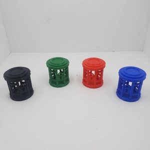 May include: Four small, cylindrical decorative cages in black, green, red, and blue. Each cage has a circular top and base, with vertical bars forming the sides. The cages are arranged in a row against a white background.
