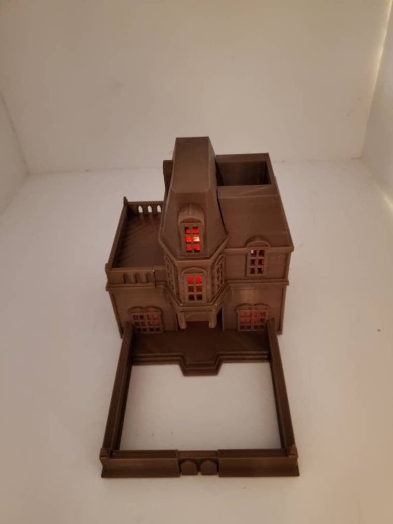 May include: A brown 3D printed model of a house with a red lit window. The house has a balcony and a small yard.
