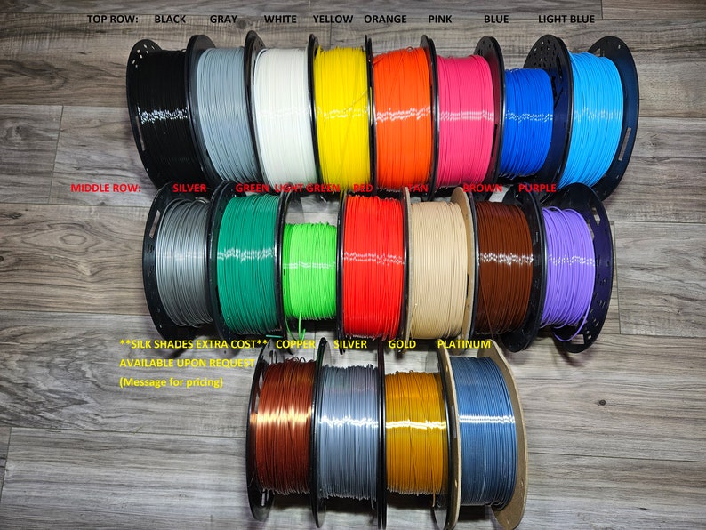 May include: Spools of filament in various colors, including black, gray, white, yellow, orange, pink, blue, light blue, silver, green, light green, red, tan, brown, purple, copper, gold, and platinum. The spools are arranged in three rows. The text "SILK SHADES EXTRA COST" is visible in the image.