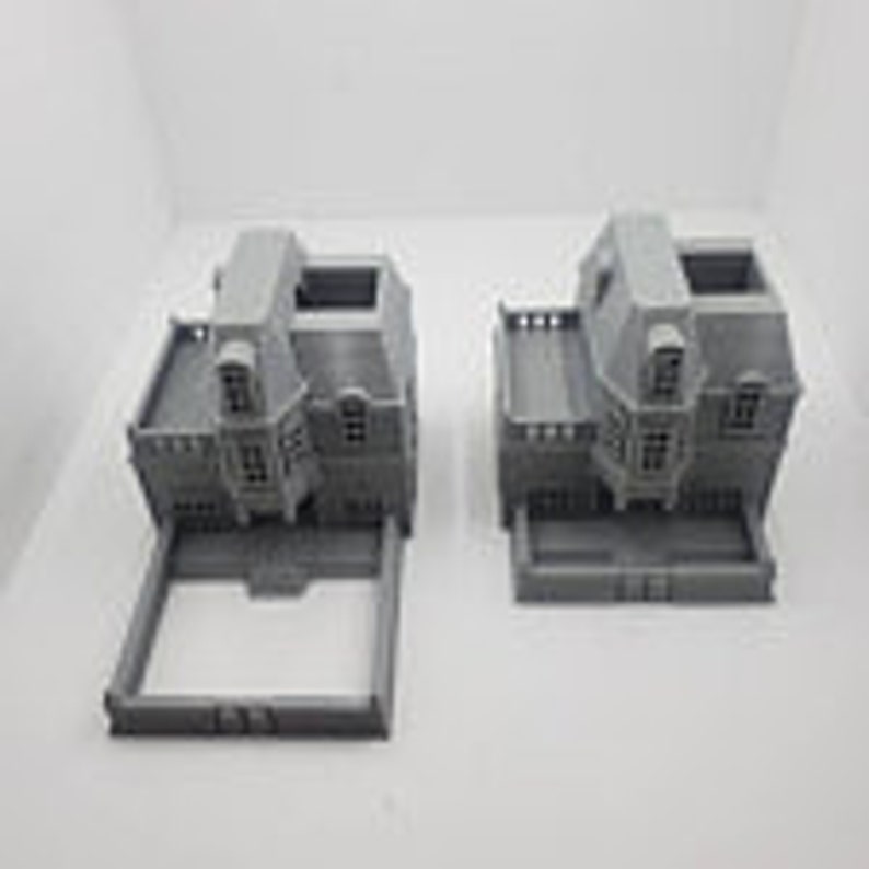May include: Two gray 3D printed miniature houses with detailed facades and open roofs. The houses have a similar design with a front porch and a second story balcony.