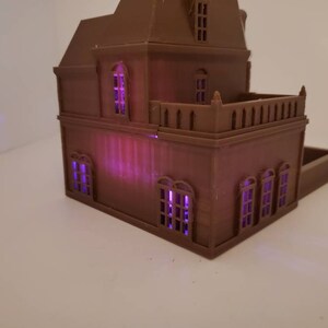 May include: A brown 3D printed model of a house with a balcony and multiple windows. The windows are lit with purple lights.