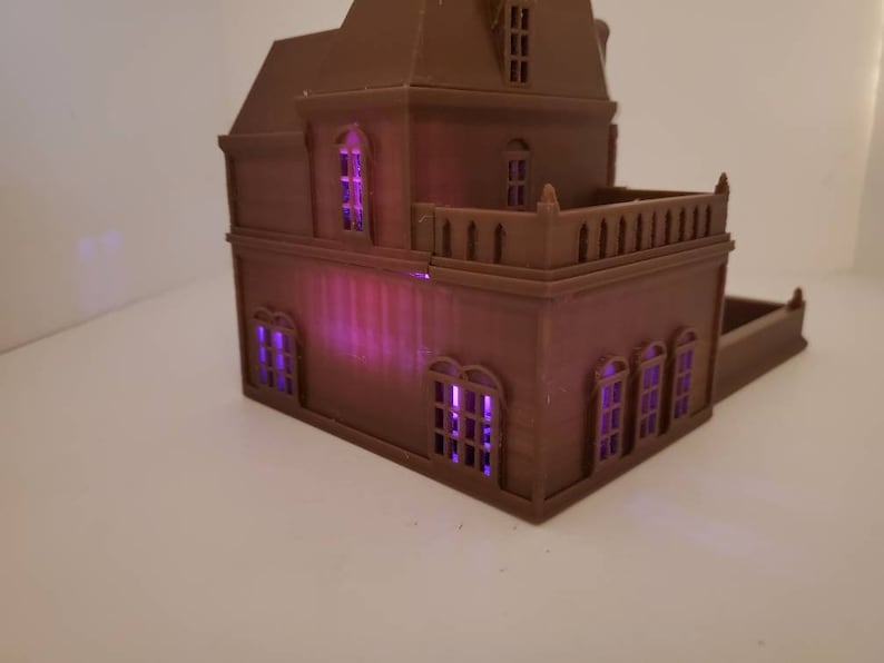 May include: A brown 3D printed model of a house with a balcony and multiple windows. The windows are lit with purple lights.