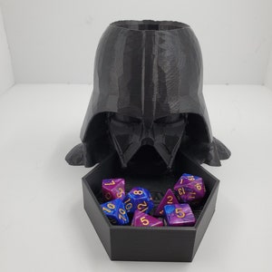 May include: A black 3D printed Darth Vader dice tower with a hexagonal dice tray. The tray is filled with blue and purple dice with gold numbers.