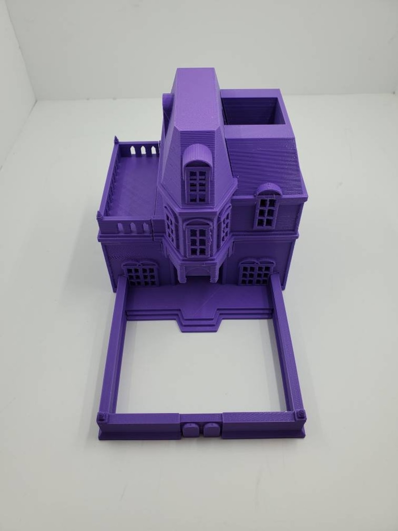 May include: A purple 3D printed model of a house with a square base and a gabled roof. The house has a balcony, windows, and a door. The model is made of plastic and is about 6 inches tall.