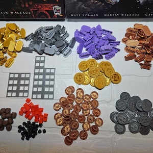 Puede incluir: Una colección de piezas de juego para un juego de mesa. Las piezas están hechas de plástico y metal y vienen en una variedad de colores, incluyendo oro, plata, morado, marrón y negro. Las piezas están dispuestas en pilas sobre una superficie blanca.
