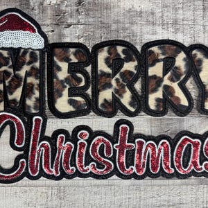 May include: A festive Christmas decoration with the words "MERRY Christmas" in a bold, eye-catching design. The word "MERRY" features a leopard print pattern, and the word "Christmas" is in red sequins. A Santa hat tops the "M" in "MERRY".