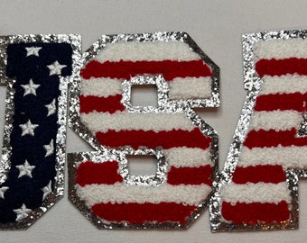 May include: USA spelled out in large, silver-trimmed letters. Each letter is made of red and white striped fabric, resembling the American flag. The "U" and "S" are blue with white stars.