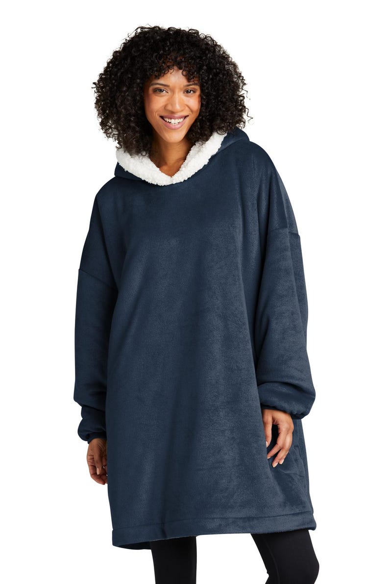 May include: A navy blue oversized hooded blanket with a white sherpa-lined hood. The blanket features long sleeves and a relaxed fit. The model is wearing the blanket. This cozy wearable blanket is designed for comfort and warmth.