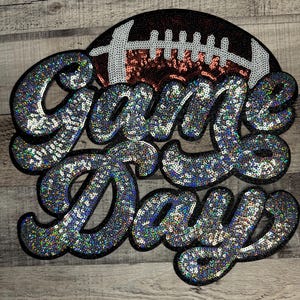 May include: A sequined patch with the words "Game Day" in a script font. The letters are covered in iridescent sequins. A football shape is behind the words, with brown and white sequins.
