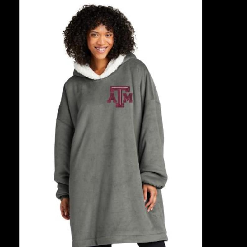 May include: A gray oversized hoodie with a white fleece-lined hood and a maroon "ATM" logo. The comfortable, long-sleeved hoodie is designed for warmth and casual wear. The soft material drapes loosely.