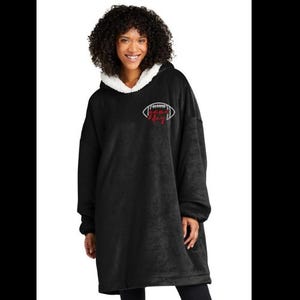 May include: Black oversized hoodie with a white sherpa-lined hood. The hoodie features a white football graphic with the text "The King" in red. The model is wearing black leggings.