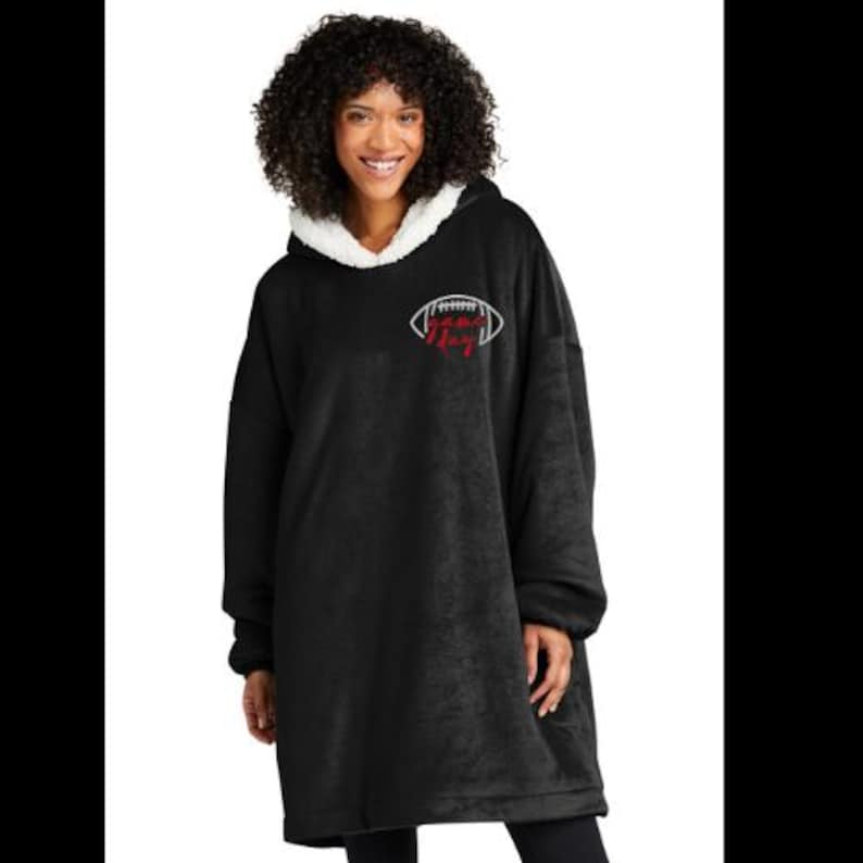 May include: Black oversized hoodie with a white sherpa-lined hood. The hoodie features a white football graphic with the text "The King" in red. The model is wearing black leggings.
