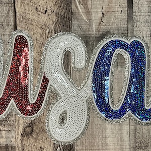 May include: USA spelled out in large, glittery letters. The U is red, the S is white, and the A is blue.