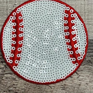 May include: A white and red baseball-shaped patch with white sequins. The patch has a red border and red stitching.