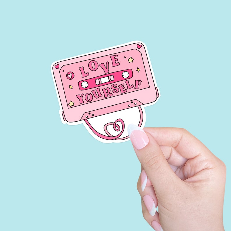 May include: Pink cassette tape sticker with the text "LOVE YOURSELF" in pink letters. The sticker has a white heart shape attached to it.