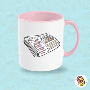May include: A white ceramic mug with a pink rim and handle. The mug features a cartoon illustration of a newspaper with the headline "Breaking News: You Deserve" and a list of positive affirmations including healing, respect, happiness, safety, kindness, and love.