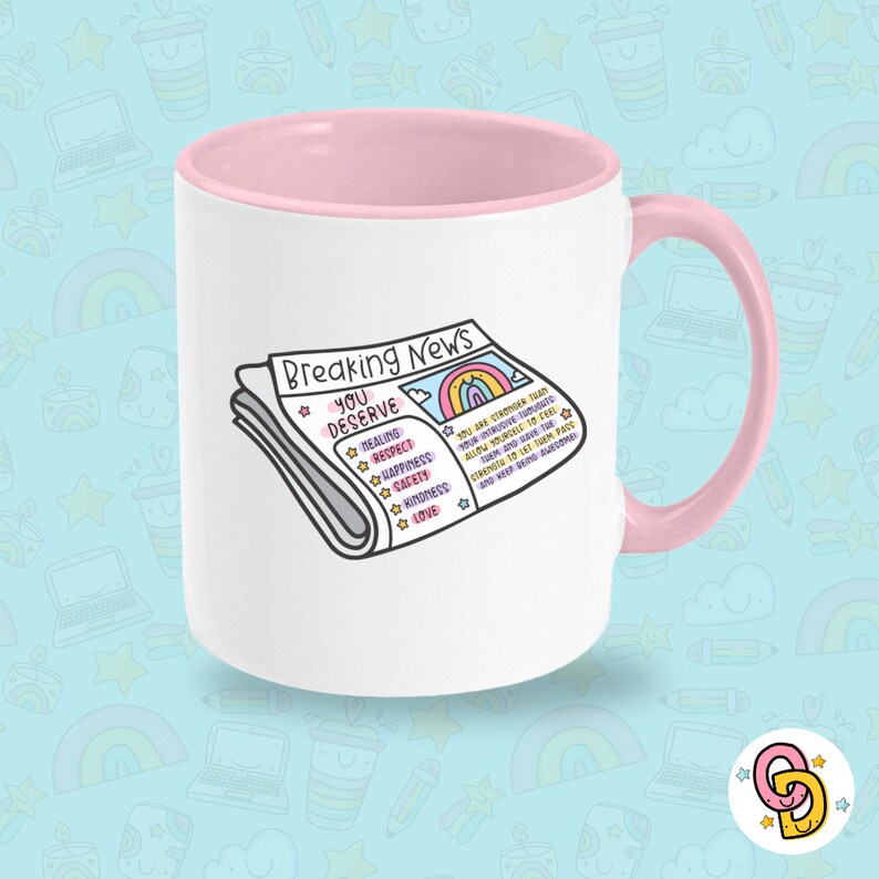 May include: A white ceramic mug with a pink rim and handle. The mug features a cartoon illustration of a newspaper with the headline "Breaking News: You Deserve" and a list of positive affirmations including healing, respect, happiness, safety, kindness, and love.