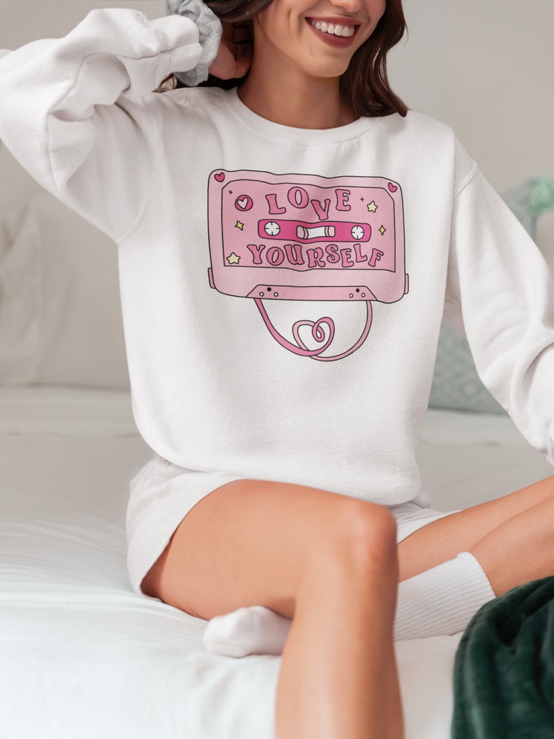 May include: White sweatshirt with a pink cassette tape graphic that says "LOVE YOURSELF" with pink stars and hearts.