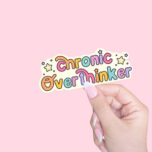 May include: A sticker with the text "Chronic Overthinker" in colorful, bubbly letters with stars around the text. The sticker is on a light pink background.