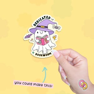 以下が含まれることがあります： 黄色い背景に、紫色の魔女の帽子をかぶってピンクの本を持っている白い幽霊。本には「DEDICATED BOOKWORM」と書かれている。