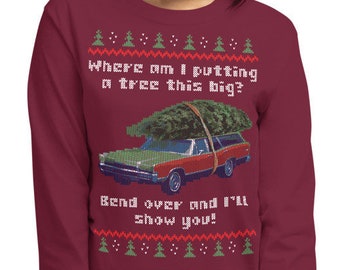 May include: A maroon long-sleeved shirt with a Christmas-themed design featuring a car with a Christmas tree on top. The text on the shirt reads "Where am I putting a tree this big? Bend over and I'll show you!"