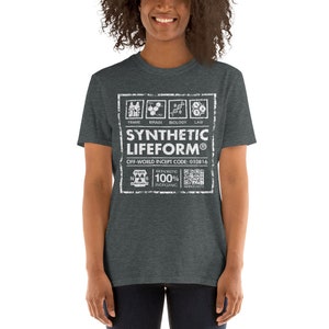 May include: A dark heather grey t-shirt with a white graphic design. The graphic features a label with the text "SYNTHETIC LIFEFORM&reg;" and "OFF-WORLD INCEPT CODE: 010816". The label also includes a diagram of a human body with the words "FRAME", "BRAIN", "BIOLOGY", and "LAW" above the diagram. Below the label is a diagram of an atom with the text "BIOROBOTIC 100% INORGANIC" and a QR code.