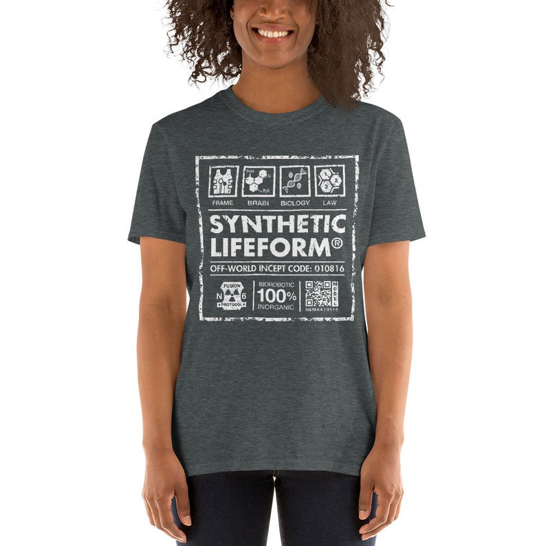 May include: A dark heather grey t-shirt with a white graphic design. The graphic features a label with the text "SYNTHETIC LIFEFORM&reg;" and "OFF-WORLD INCEPT CODE: 010816". The label also includes a diagram of a human body with the words "FRAME", "BRAIN", "BIOLOGY", and "LAW" above the diagram. Below the label is a diagram of an atom with the text "BIOROBOTIC 100% INORGANIC" and a QR code.