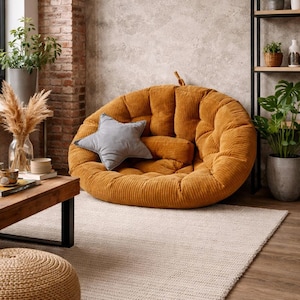 May include: A large, round, mustard-colored corduroy floor cushion with a gray star-shaped pillow and a smaller bolster pillow. The cushion is in a living room setting with a neutral rug and wooden furniture.