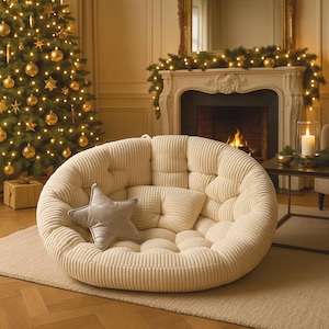 May include: A cream corduroy floor chair, round with a tufted design. It has a small, rectangular pillow and a grey star-shaped pillow. The chair is in a room with a Christmas tree and a fireplace.