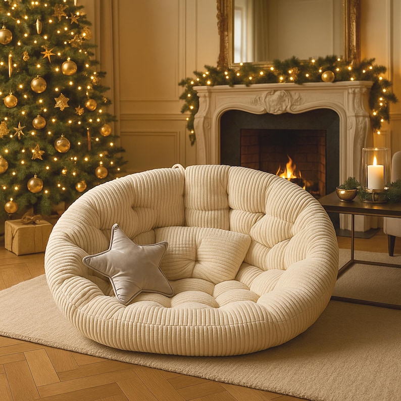 May include: A cream corduroy floor chair, round with a tufted design. It has a small, rectangular pillow and a grey star-shaped pillow. The chair is in a room with a Christmas tree and a fireplace.