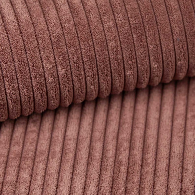 May include: Close-up of a section of brown corduroy fabric. The fabric has a ribbed texture with vertical lines. The color is a muted, earthy brown, and the fabric appears soft and plush.