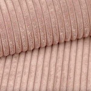May include: Close-up of a section of corduroy fabric in a soft, muted rose color. The fabric has a ribbed texture with vertical lines, creating a plush and tactile appearance. The corduroy is folded over, showing the texture and depth of the material.