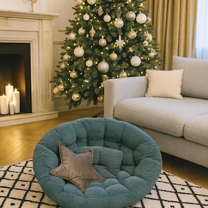 May include: A teal corduroy round chair with a star-shaped pillow sits on a patterned rug. A decorated Christmas tree with gold ornaments and lights is in the background, along with a gray sofa and fireplace.