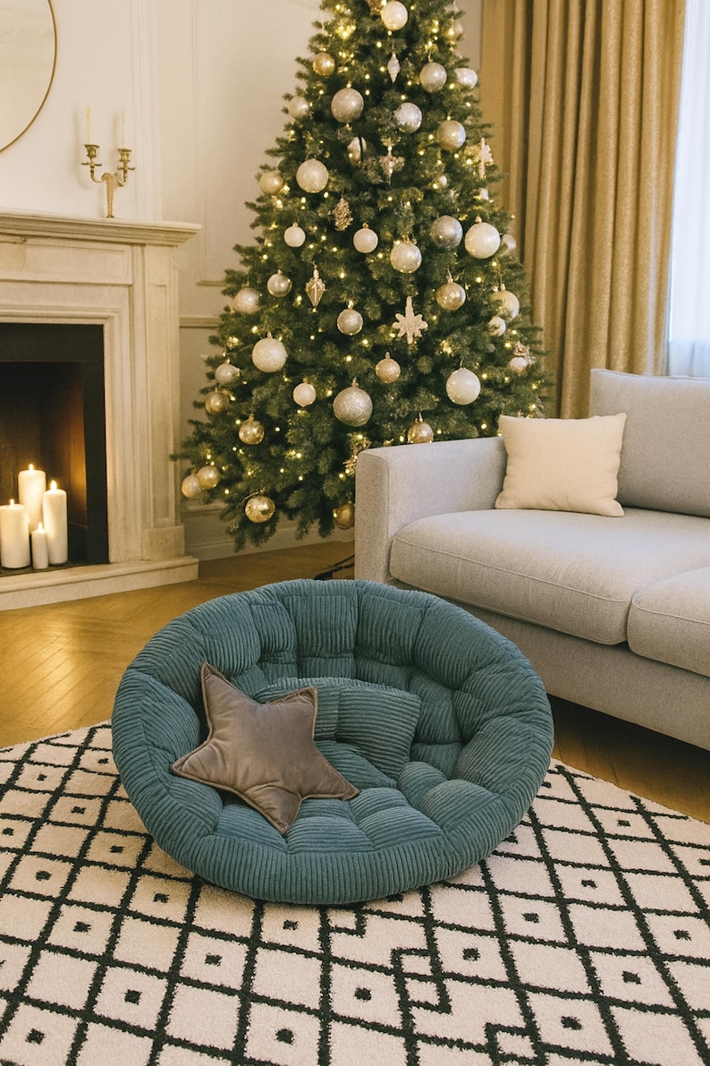 May include: A teal corduroy round chair with a star-shaped pillow sits on a patterned rug. A decorated Christmas tree with gold ornaments and lights is in the background, along with a gray sofa and fireplace.