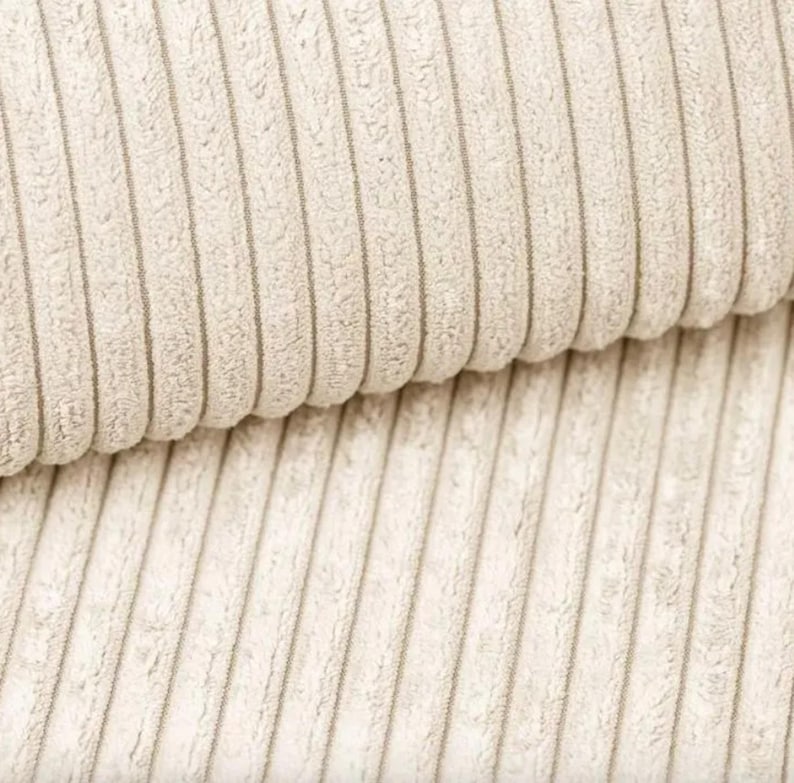 May include: Close-up of a beige corduroy fabric with vertical ridges. The fabric has a soft, textured appearance and a neutral color, suitable for various textile projects. The ridges create a pattern of light and shadow.