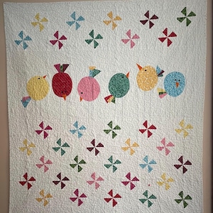 May include: A handmade quilt featuring colorful, stylized birds perched on thin stems. The birds are various colors, including yellow, red, pink, and blue, with patterned bodies. Scattered pinwheel designs in multiple colors adorn the white background.