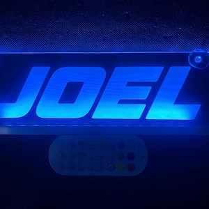 May include: A blue LED sign with the name "JOEL" in white lettering. The sign is illuminated with a bright blue light and has a remote control.