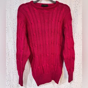 May include: A deep crimson red cable knit jumper with a crew neck. The jumper has a textured pattern and is made of a soft, warm material.