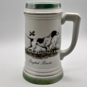 May include: White ceramic beer stein with a green rim and handle. The stein features a black and white English Pointer dog illustration with the words "English Pointer" below the image. A small bird is also depicted.