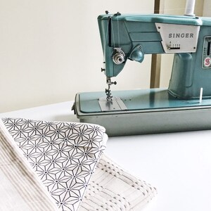 May include: A vintage teal blue Singer sewing machine with a white bobbin on top, sitting on a white table with a folded fabric with a geometric pattern.