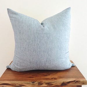 May include: A light blue throw pillow with a subtle textured fabric. The pillow is sitting on a wooden surface.