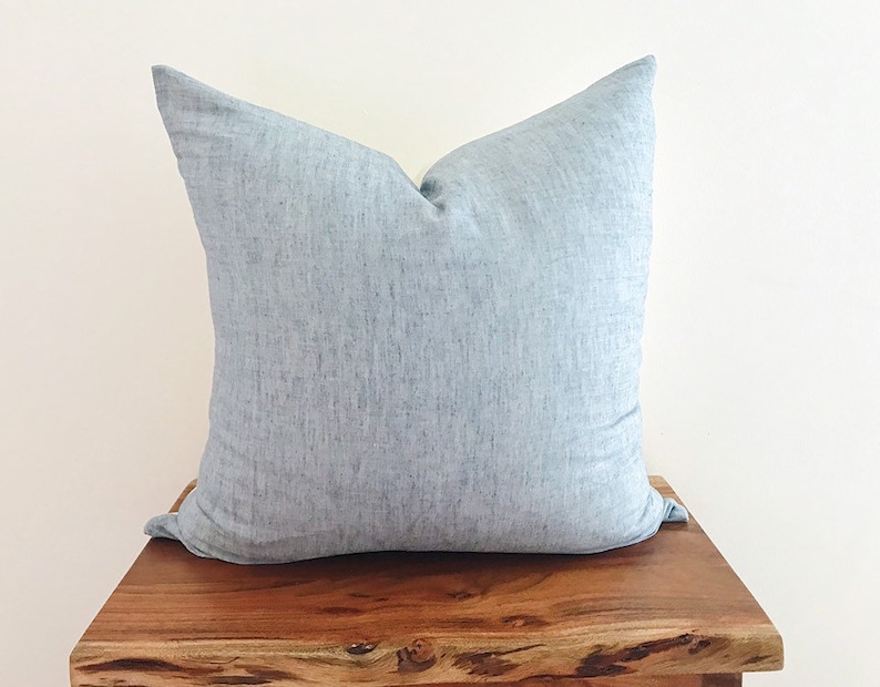 May include: A light blue throw pillow with a subtle textured fabric. The pillow is sitting on a wooden surface.