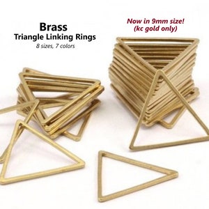 May include: Brass triangle linking rings in various sizes. The rings are stacked and arranged in a pile. The text "Now in 9mm size! (kc gold only)" is written above the pile of rings.